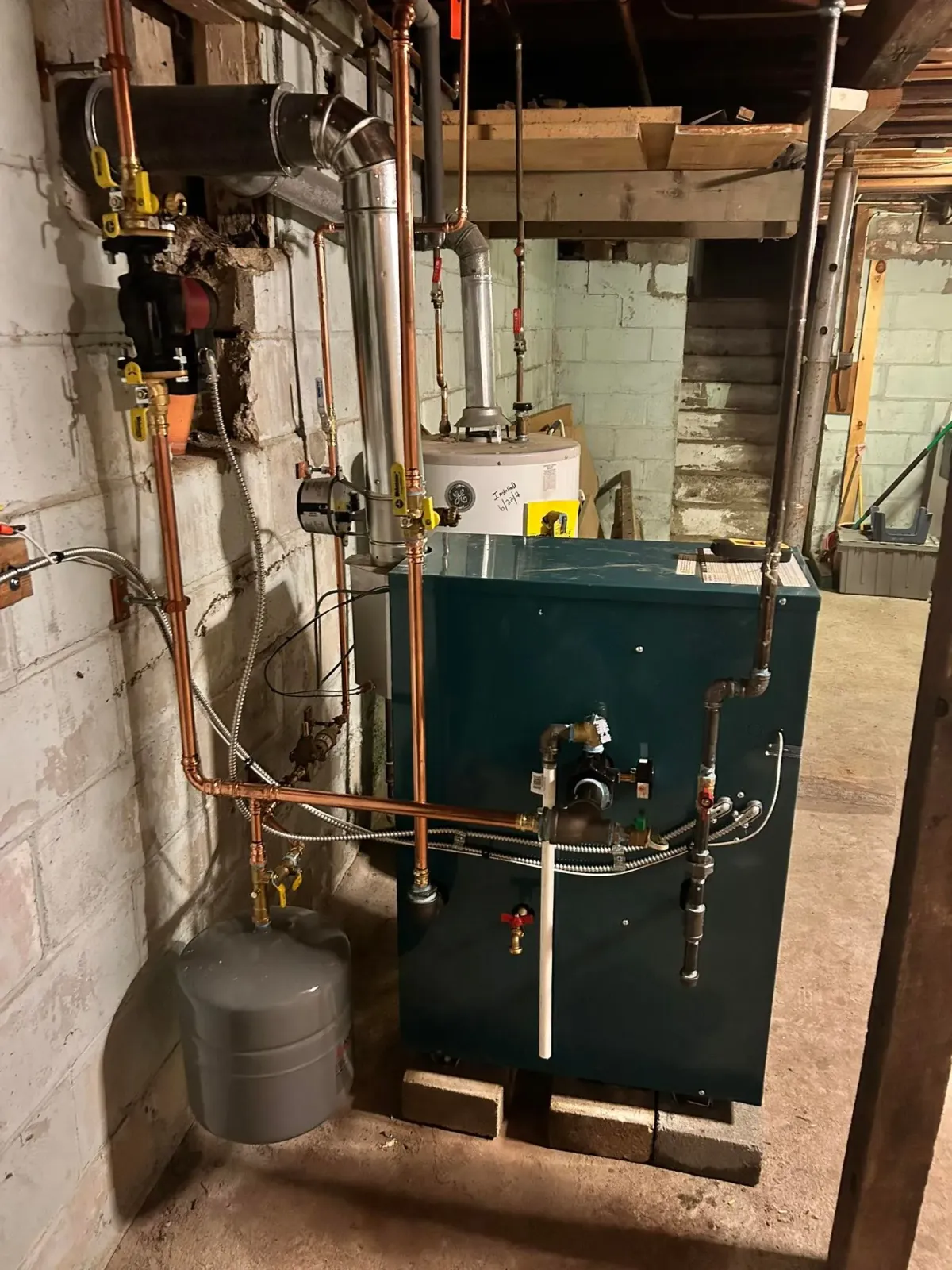 A boiler is sitting in a basement next to a brick wall.