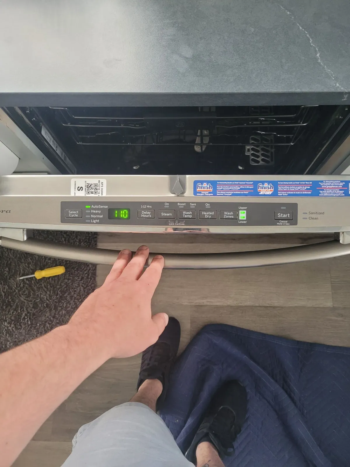 A person’s hand reaches toward the control panel of an open dishwasher in a kitchen.