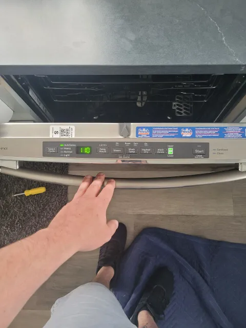 A person’s hand reaches toward the control panel of an open dishwasher in a kitchen.